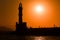 Silhouette of tourists on a Venetian harbor wall next to a lighthouse watching a spectacular sunset