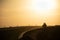 Silhouette of a tractor leveling the newly-laid asphalt on a road under a bright sky at sunset