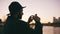 Silhouette of traveler man in hat taking panoramic photo of the city skyline on his smartphone camera at sunset