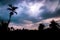 A silhouette of trees and houses with orange sky full of dark blue clouds above. Calmness before the storm