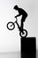 silhouette of trial biker performing stunt while balancing on cube