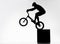 silhouette of trial cyclist performing back wheel stand while balancing on cube