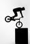 silhouette of trial cyclist performing nollie while balancing on cube