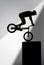 silhouette of trial cyclist performing stunt while balancing on cube