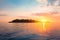 Silhouette of tropical island surrounded by water on horizon, sunset