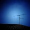 Silhouette of TV antenna installed on roof with dark blue sky background.