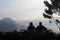 Silhouette of Two couple elderly people sitting on wooden bench and seeing view in the morning with mountain background