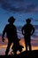 Silhouette of two cowboys in the sunset one hold saddle