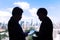 Silhouette of two executive businessmen discussing over a project on a computer tablet with city highrises and sky view in the ba