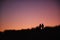 Silhouette Of Two Female Friends Walking Across Dunes Against Setting Sun