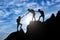 Silhouette of two female mountaineers helping another female mountaineer to overcome the obstacle in the mountains