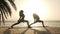 Silhouette of two women practice warrior yoga posture at seaside in sunshine