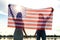 Silhouette of two young friends women holding USA national flag in their hands standing together outdoors. Patriotic girls