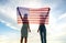 Silhouette of two young friends women holding USA national flag in their hands at sunset. Patriotic girls celebrating United
