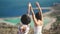 Silhouette of two young girls standing on cliff with the view on blue sea lagoon holding their hands in the air. Women