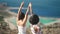 Silhouette of two young girls standing on cliff with the view on blue sea lagoon holding their hands in the air. Women