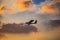 Silhouette of ultralight microlite aircraft flying with a pilot and a passenger against sunset sky