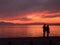 Silhouette of unidentifiable couple before an orange sunset by the waterfront.
