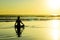 Silhouette of unknown unrecognizable woman sitting on beach sea water practicing yoga and meditation looking to the sun on the hor