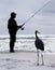 Silhouette of an Unrecognizable Fisherman on a Florida Beach with a Hopeful Great Blue Heron Looking On