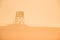 A silhouette of a watchtower in a landscape in the morning sunset. The whole pictures is in a golden orange colour.