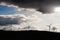 Silhouette of wind farm electricity generators over dark forest. Dramatic cloudy sky. Sun flare. Copy space. Green renewable