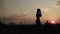 Silhouette woman against the background of sunset makes blows in the air taking steps forward, side view. Woman trains