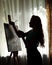 Silhouette woman artist draws paint picture on easel