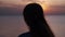 Silhouette of a woman on a background of sunset by the sea. The figure of a girl in the rays of the setting sun on the beach