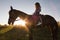 Silhouette of a woman in cowboy hat riding a horse - sunset or sunrise, horizontal