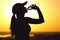 Silhouette of a woman drinking water after physical exercise in nature, sports female profile at sunset, concept of sport and rela