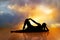 Silhouette of a woman exercising yoga on wooden floor with the vibrant sky