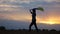 Silhouette of woman goes with raised flag of Ukraine above head on wheat field. Ukrainian lady walking with national