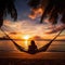 Silhouette of woman in a hammock on the beach watching a spectacular sunset.