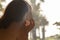 Silhouette of woman with headphones lying on the sunbed on terrace and looking on palm trees sea beach at sunset. Female relaxing