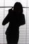 Silhouette of woman looking through the blind