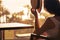 Silhouette of woman puts on straw hat sitting on the armchair near table on balcony and looking on sunset palm sea beach.