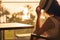 Silhouette of woman puts on straw hat sitting on the armchair near table on balcony and looking on sunset palm sea beach. Rear