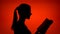 Silhouette of woman reading physical print book on red background. Female`s face in profile studying