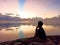 Silhouette of a woman sitting alone on the beach, enjoying the tranquil view over the sea surrounded with colorful sky light.