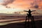 A silhouette woman sitting on a lifeguard tower with open arms enjoying the sunrise on a beach and the sun`s rays painting the sky