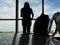 Silhouette woman stand and look outside window with bag on chair waiting flight in airport. Woman travel alone