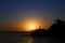 Silhouette of a woman standing at the breakage at the rosky beach at the sunset