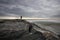 Silhouette of a woman standing on a jetty as the sunsets over the ocean.