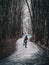 Silhouette of a woman with an umbrella walking along a winding path in a spring Park under wet snow. Dark tone