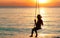 Silhouette woman wear bikini and straw hat swing the swings at the beach on summer vacation at sunset. Enjoying and relaxing girl