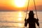 Silhouette woman wear bikini and straw hat swing the swings at the beach on summer vacation at sunset. Enjoying and relaxing girl