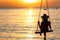 Silhouette woman wear bikini and straw hat swing the swings at the beach on summer vacation at sunset. Girl in swimwear sit