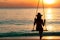 Silhouette woman wear bikini and straw hat swing the swings at the beach on summer vacation at sunset. Girl in swimwear sit