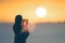 Silhouette of woman with wet hair wrapped in a blanket after swimming. Female taking picture on mobile phone standing on the beach